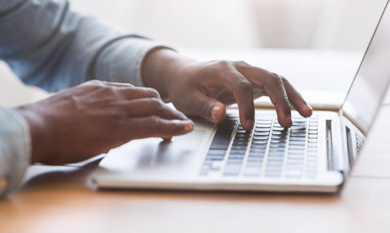 Close-up of the hands of an African-American businessman typing on a laptop keyboard.